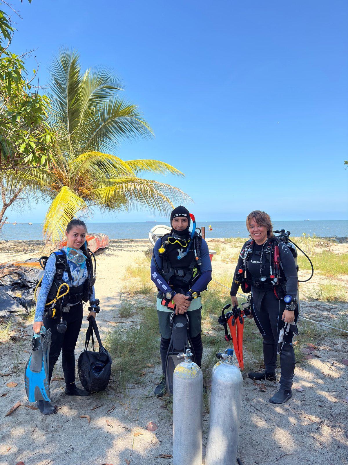 Tres integrantes del equipo con equipo de buceo en la playa